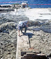 archéologue examinant et effectuant les relevés sur les vestiiges de l'ancienne centrale Brown. à l'arrière plan, le Saint-Maurice